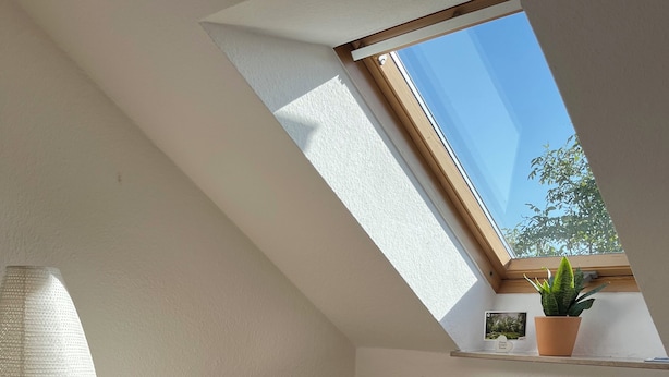 Quarto com claraboia, cómoda de madeira, mesa de cabeceira, luminária e planta em vaso.