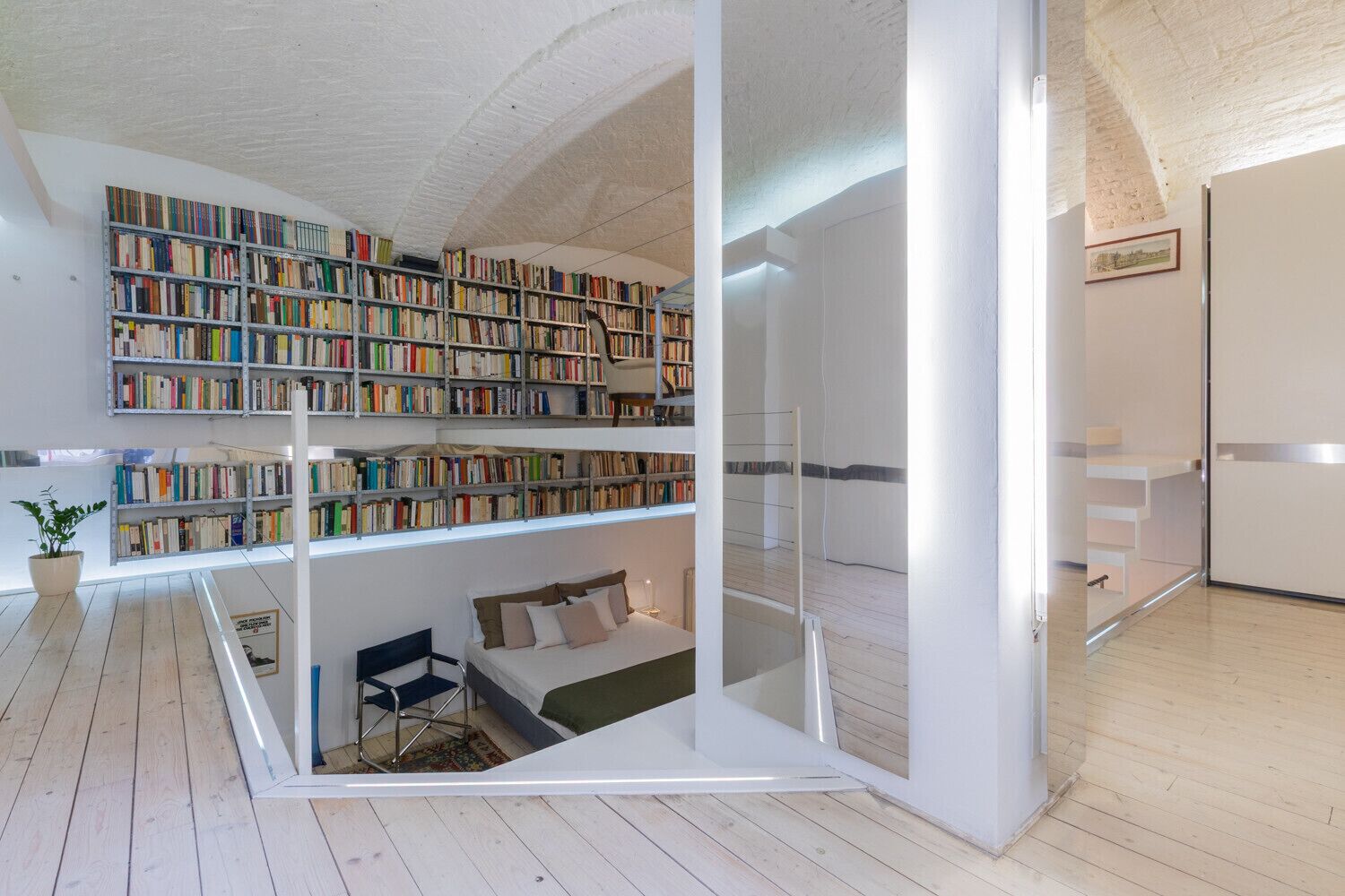 A modern room with a loft bed, a large bookshelf, and a glass partition.