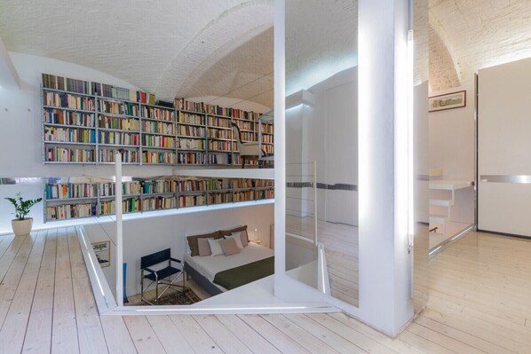 A modern room with a loft bed, a large bookshelf, and a glass partition.