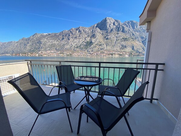 A balcony with four chairs and a table, overlooking a lake with mountains in the background.