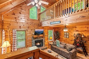 A cozy cabin interior with a fireplace, a sofa, a television, and a balcony. - Spacious cabin, Pigeon Forge-GSMNP-Relaxing & fun (Sevierville)