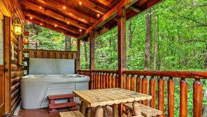 A wooden deck with a hot tub, picnic tables, and a view of a forest. - Spacious cabin, Pigeon Forge-GSMNP-Relaxing & fun (Sevierville)