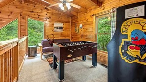 A wooden interior with a foosball table, a ceiling fan, and large windows. - Spacious cabin, Pigeon Forge-GSMNP-Relaxing & fun (Sevierville)