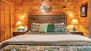 A wooden cabin-style bedroom with a bed, two bedside lamps, and a 'Be still' sign on the wall. - Spacious cabin, Pigeon Forge-GSMNP-Relaxing & fun (Sevierville)