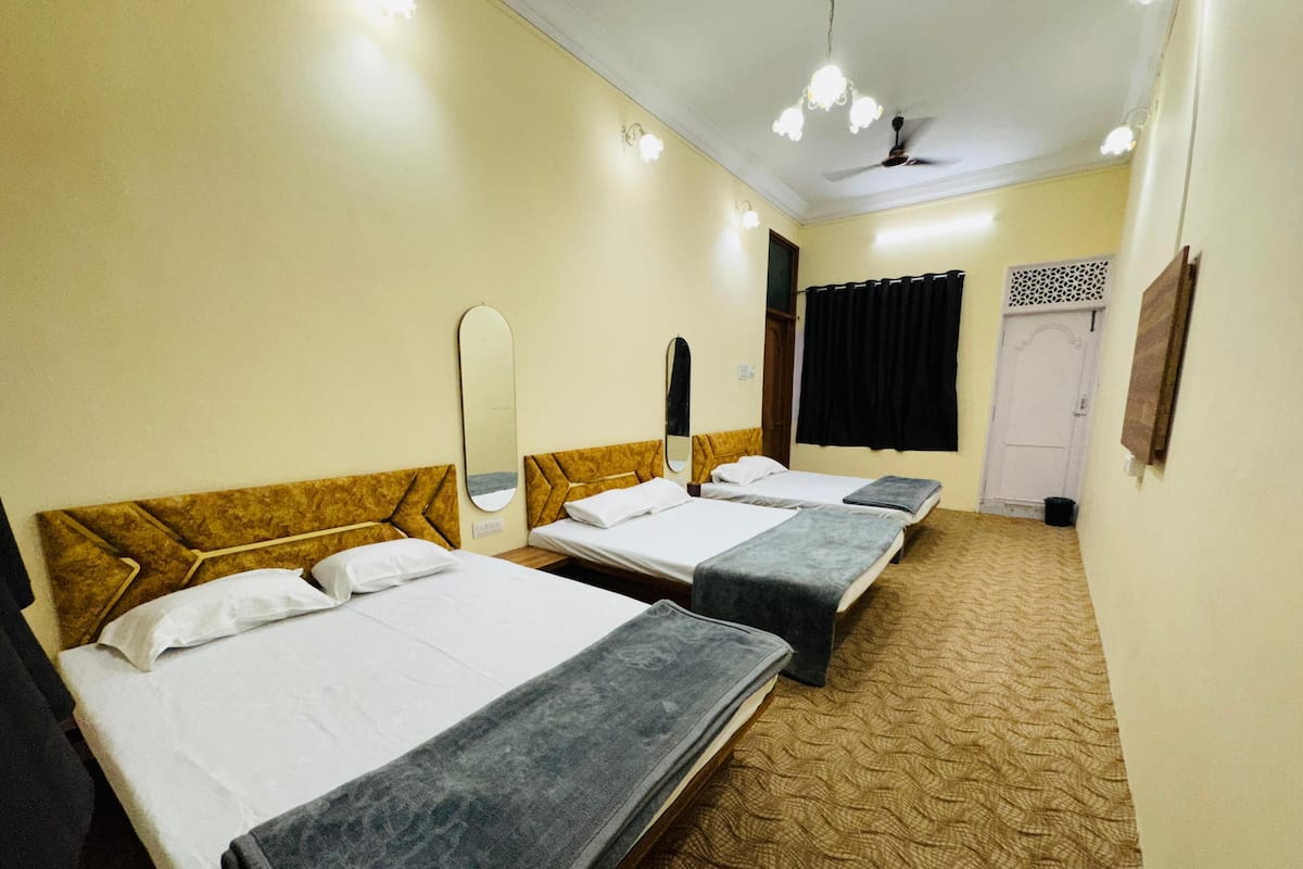 Une chambre d’hôtel avec trois lits simples, un ventilateur de plafond et une moquette à motifs.