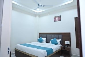 A neatly arranged bedroom with a bed, bedside table, and a ceiling fan. - Kusum Dham By Reverie (Vrindavan)