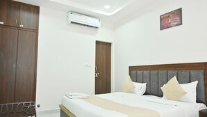 A hotel room with a bed, a wardrobe, an air conditioning unit, a door, and a wall-mounted picture. - Kusum Dham By Reverie (Vrindavan)