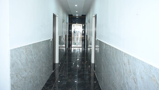 A hallway with marble walls and black tiled floor, leading to a glass door entrance. - Kusum Dham By Reverie (Vrindavan)