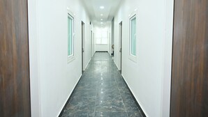 A long, narrow hallway with white walls and dark wooden doors. - Kusum Dham By Reverie (Vrindavan)