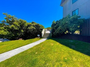 Un edificio con una escalera que conduce a una puerta, rodeado de césped cuidado y árboles.