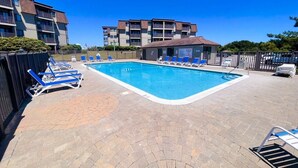 Ein Schwimmbecken mit Liegestühlen, einer Pflasterterrasse und Wohngebäuden im Hintergrund.