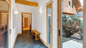 Un pasillo con vigas de madera, un banco y una puerta que da a un balcón con vistas a árboles.