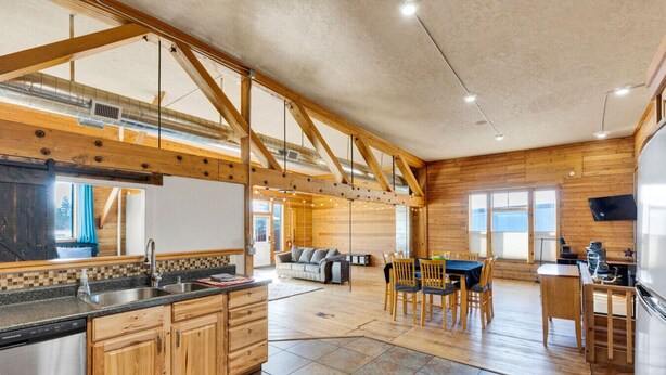 A spacious kitchen with wooden cabinets, a dining area with a table and chairs, and a living room with a sofa. - The Bitterroot Loft On 1st Street (Hamilton)