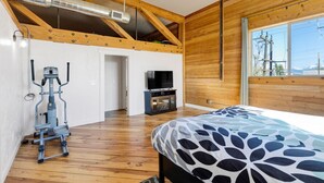 A bedroom with a bed, a TV, wooden walls, a ceiling fan, and a workout machine. - The Bitterroot Loft On 1st Street (Hamilton)