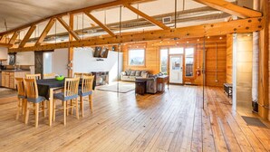A spacious loft-style room with a high ceiling, exposed wooden beams, a dining area with a table and chairs, a seating area with a sofa, and a large window providing natural light. - The Bitterroot Loft On 1st Street (Hamilton)