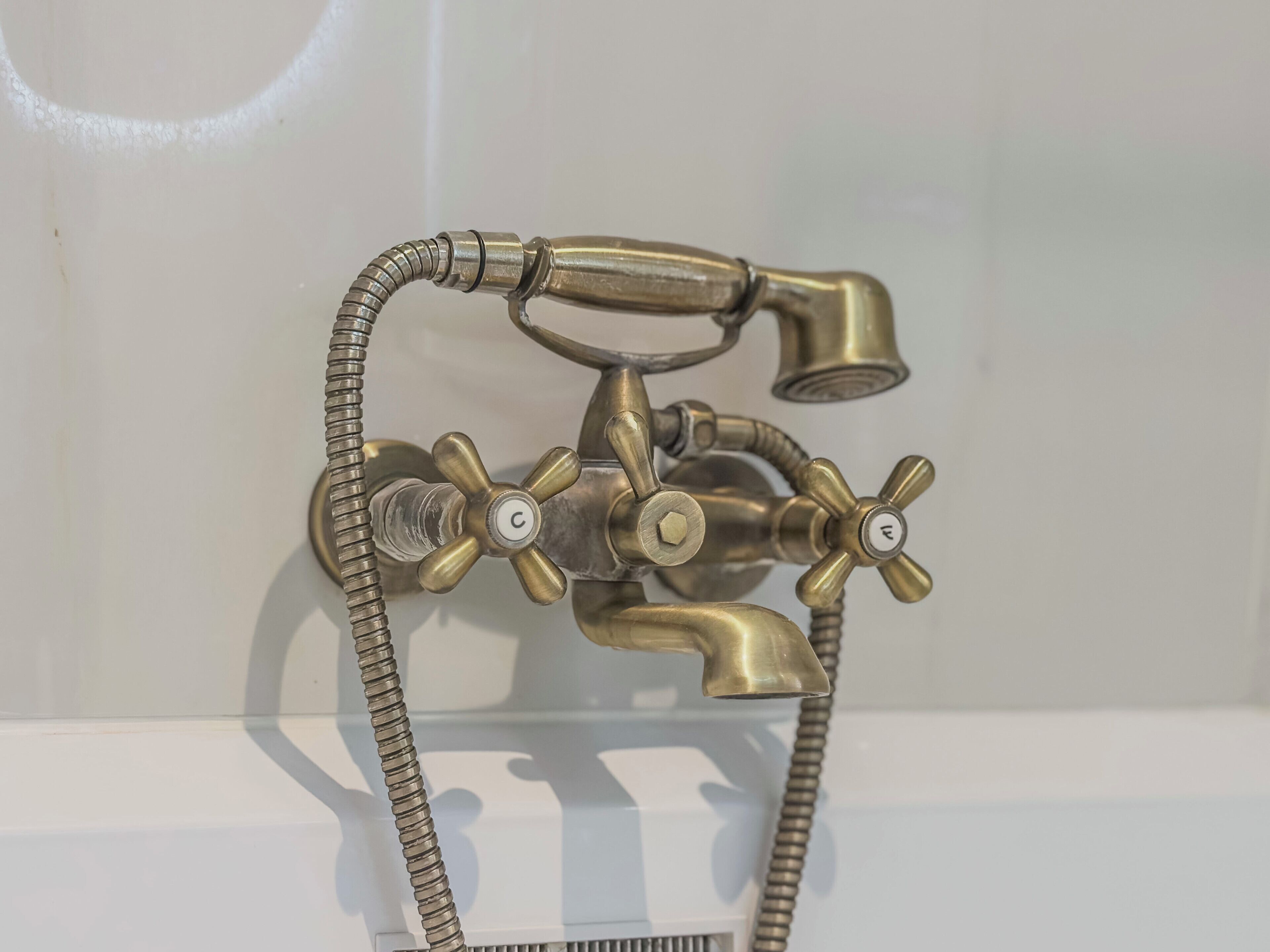 A brass bathroom fixture with multiple spouts and a flexible hose.