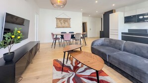 A modern living room with a sofa, a dining table with chairs, a TV, and a kitchen area with cabinets and a stove. - #HU | Le Coeur Lorraine 🥐  | City center/Station T3 (Grenoble)