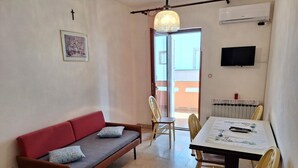 A furnished room with a sofa, dining table, chairs, a TV, and a radiator. - apartman Štefica 2 with AC and WIFI (Punat)