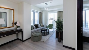 Een moderne hotelkamer met een bank, een ronde salontafel, een bureau met spiegel, en een groot raam met uitzicht op de stad.