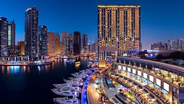 Een hotel aan het water met meerdere balkons, een jachthaven met boten, en een stadsachtergrond.