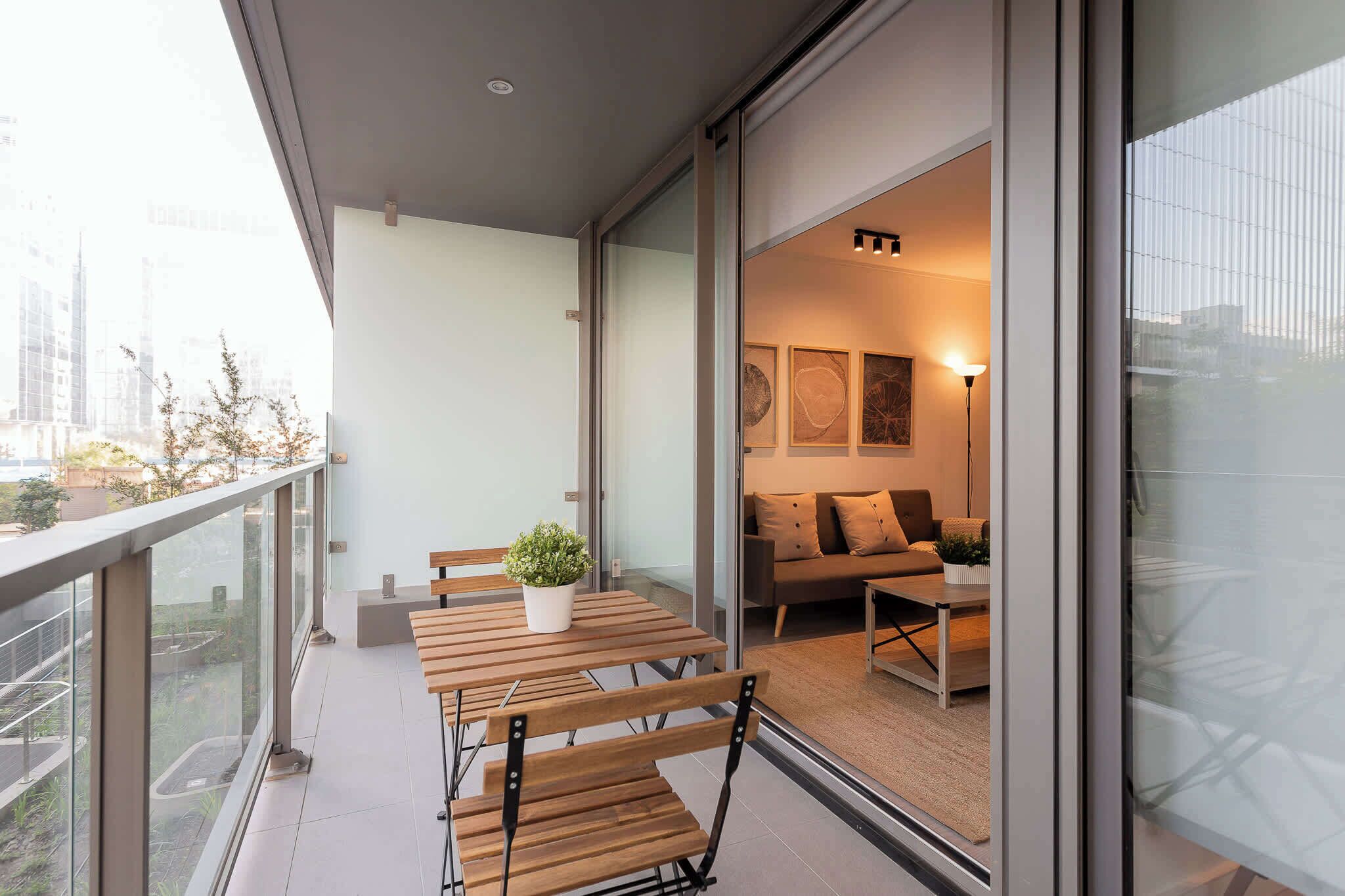Ein Balkon mit Holztisch und -stühlen, einem Blumentopf und Blick auf die Stadtlandschaft.