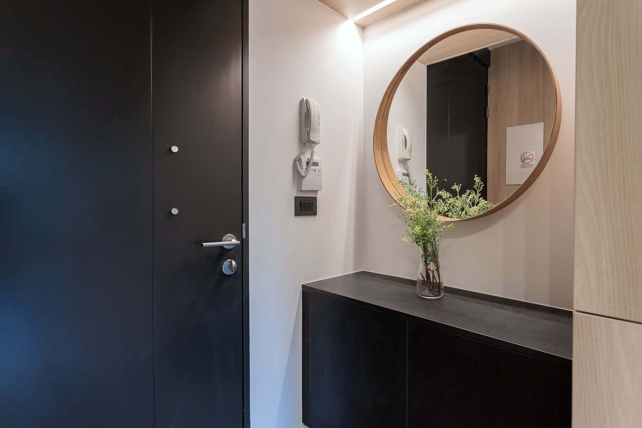 A modern bathroom with a dark door, a round mirror, a telephone, and a small plant on a black vanity.