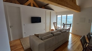 A living room with a sofa, a television, and a balcony with wicker chairs. - Luxury Douro Villa | Private pool, river views & BBQ Terrace (Vila Marim, Mesão Frio)