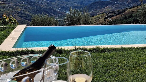 A table with a glass of white wine, a glass of white wine, and a platter of cured meats and cheese, with a pool and mountainous landscape in the background. - Luxury Douro Villa | Private pool, river views & BBQ Terrace (Vila Marim, Mesão Frio)