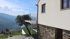 A modern house with a stone foundation, a balcony, and a view of a valley and mountains. - Luxury Douro Villa | Private pool, river views & BBQ Terrace (Vila Marim, Mesão Frio)