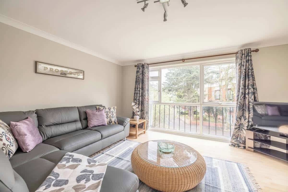 A living room with a sofa, a round coffee table, a TV, and a large window with curtains.
