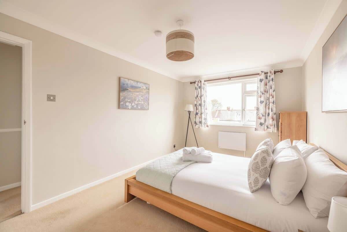 A bedroom with a bed, a window with curtains, a bedside lamp, and a painting on the wall.