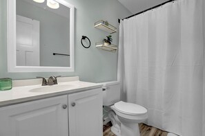 A bathroom with a white sink, a toilet, a shower curtain, and a mirror. - Stunning Second Row Duplex, Easy Beach Access, Pet-friendly (North Topsail Beach)