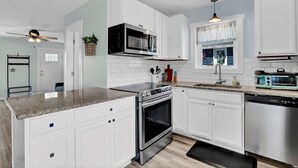 Une cuisine moderne avec des meubles blancs, des appareils en acier inoxydable, un plan de travail en granit et un ventilateur de plafond.