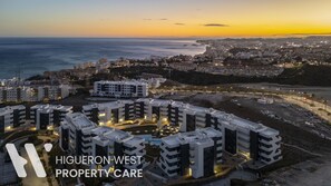 Un ensemble immobilier résidentiel de grande hauteur, doté de nombreux balcons, d’une cour intérieure et offrant une vue sur la mer et le paysage urbain.