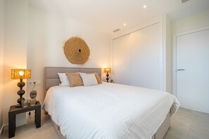 A neatly arranged bedroom with a large bed, two bedside tables with lamps, and a wall-mounted decorative item. - The Panorama Penthouse – Penthouse with Pool and Sea Views | Fuengirola (Fuengirola)