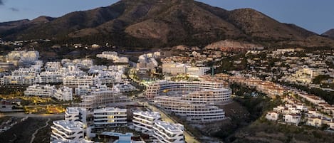 Stunning coastal town with modern apartments and houses, set against a majestic mountain backdrop.