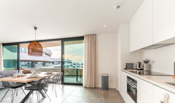 A modern kitchen with a dining area, large windows, and a view of the cityscape. - La Calma Sur – Sunny South-Facing Terrace with Pool Views | Fuengirola (Fuengirola)