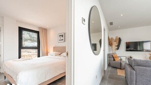 A modern bedroom with a large bed, a view of the beach, and a living area with a sofa and TV. - La Calma Sur – Sunny South-Facing Terrace with Pool Views | Fuengirola (Fuengirola)