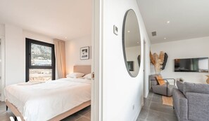 A modern bedroom with a large bed, a view of the beach, and a living area with a sofa and TV. - La Calma Sur – Sunny South-Facing Terrace with Pool Views | Fuengirola (Fuengirola)