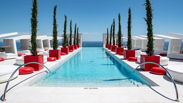 A pool area with a clear blue pool, red and white seating, and tall green trees. - La Vida Feliz Andalucia – Andalusian Garden, Sea Views | Higueron West, Fuengirola (Fuengirola)