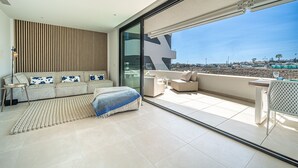 A modern living room with a sofa set, a coffee table, and a large glass door leading to a balcony with a view of the beach and cityscape. - La Vida Feliz Andalucia – Andalusian Garden, Sea Views | Higueron West, Fuengirola (Fuengirola)