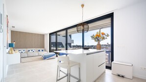 A modern kitchen with a large island, a dining area with a white chair, and a view of the city through large windows. - La Vida Feliz Andalucia – Andalusian Garden, Sea Views | Higueron West, Fuengirola (Fuengirola)