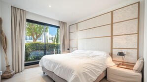 A modern bedroom with a large bed, a nightstand, a lamp, and a view of greenery outside. - Garden Villa - Large Terrace with Outdoor Kitchen and Pool, Higueron West, Fuengirola (Fuengirola)