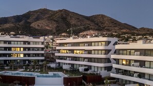 Et moderne hotel med flere etager, en pool på taget og et bjergrigt landskab i baggrunden.