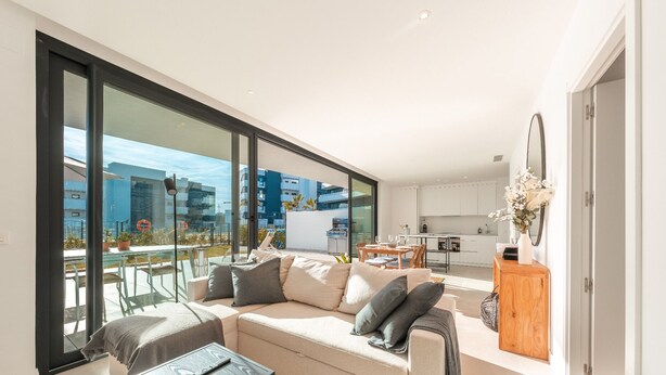 En moderne lejlighed med stor balkon, sofa, spisebord og et køkkenområde.