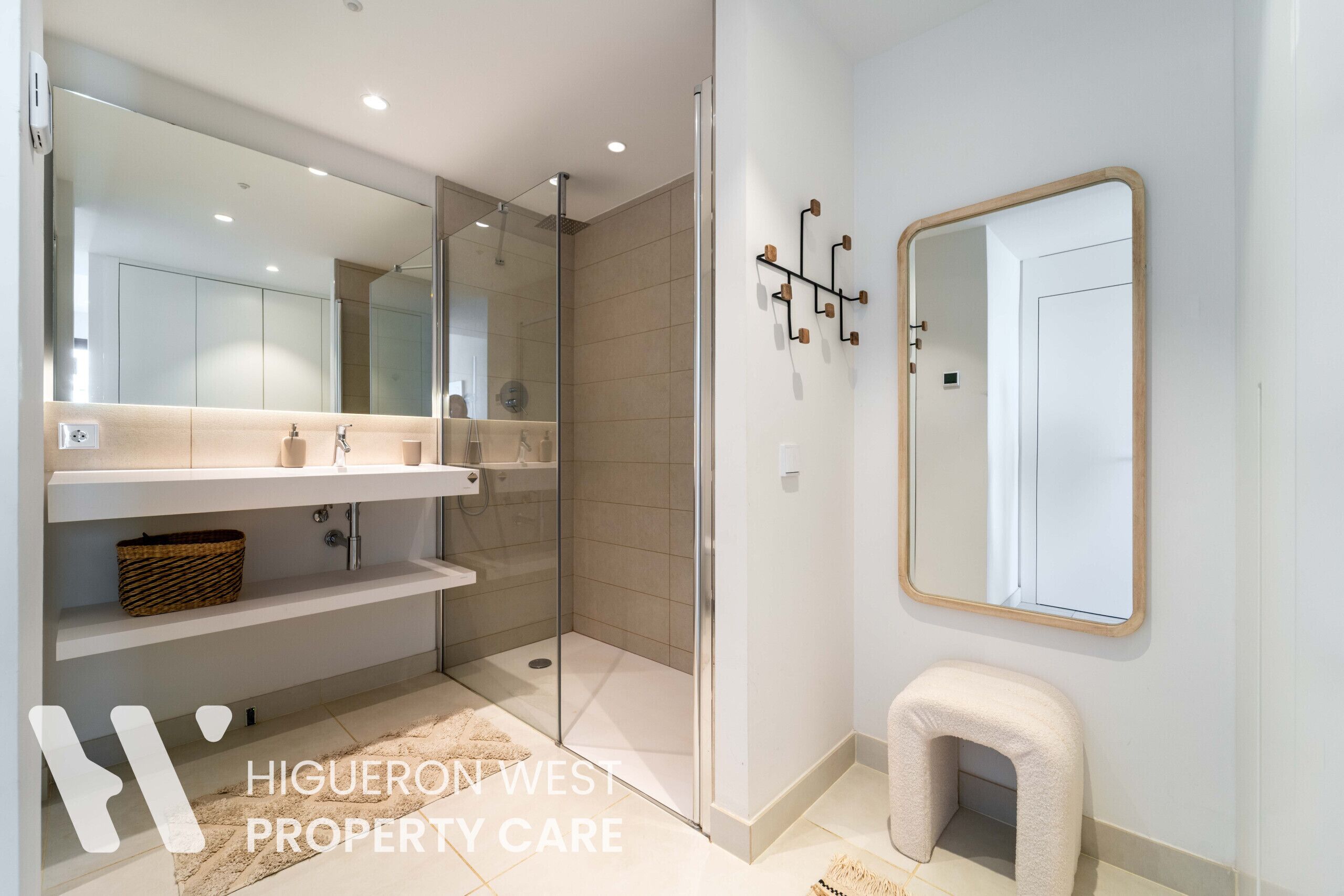 A modern bathroom with a glass-enclosed shower, a large mirror, and a small stool.