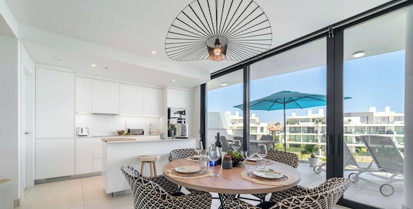 A modern kitchen with white cabinets, a dining area with patterned chairs, and a large window with a view of buildings.
