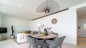 Een moderne eethoek met een ronde tafel, zwart-wit gestreepte stoelen, een plafondventilator en een flatscreen televisie op de achtergrond.