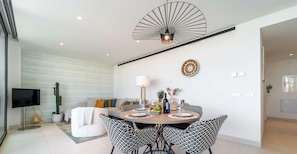 A modern dining area with a round table, black and white patterned chairs, a ceiling fan, and a flat-screen TV in the background.