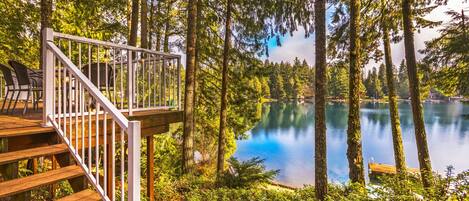 A wooden deck with a railing overlooking a lake surrounded by tall trees.